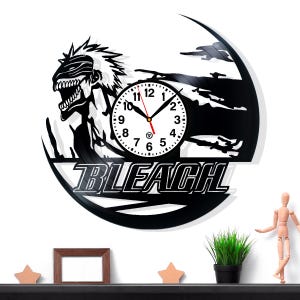 Op de afbeelding: Zwarte wandklok met een anime-personage en het woord "BLEACH". De klok heeft een witte wijzerplaat met zwarte cijfers en wijzers. De klok is gemaakt van een gerecyclede vinylplaat.