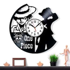 May include: Black vinyl record clock featuring a character illustration and the text "One Piece." The clock face is white with black numbers and hands. The design includes a skull and crossbones symbol.