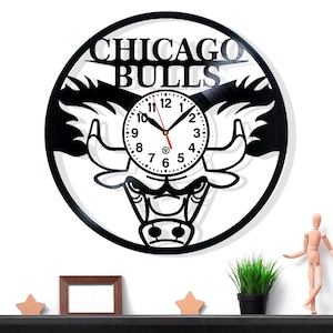 May include: Black Chicago Bulls wall clock with a white clock face. The clock features the team's logo and the words "CHICAGO BULLS" at the top. The clock hands are black and red.