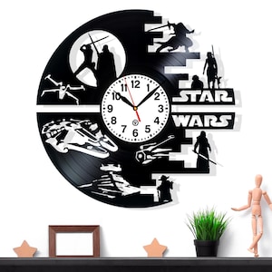 May include: Black Star Wars themed wall clock made from a vinyl record. The clock features iconic characters and spacecraft silhouettes, with a white clock face and hands. The clock measures approximately 12 inches in diameter.