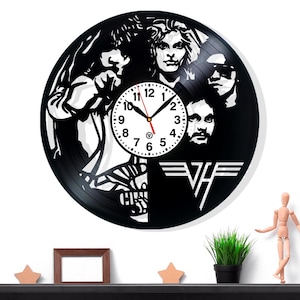 Könnte beinhalten: Schwarze Vinyl-Schallplattenuhr mit Porträts und Logo einer Band. Das Zifferblatt ist weiß mit schwarzen Zahlen und Zeigern. Die Bandmitglieder sind weiß vor dem schwarzen Hintergrund der Schallplatte dargestellt. Ein dekorativer Artikel.