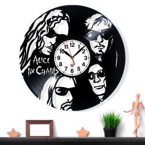 Puede incluir: Un reloj de vinilo negro con la banda Alice in Chains. La esfera del reloj es blanca con números y manecillas negras. Las caras de los miembros de la banda están silueteadas en blanco sobre el disco negro.