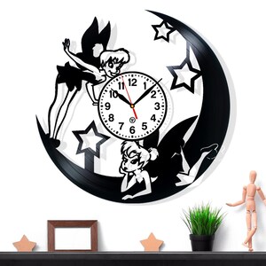 May include: Black vinyl record clock featuring a fairy design with a crescent moon and stars. The clock face is white with black numbers and hands. The fairy is depicted in a whimsical style, adding a touch of fantasy to the decor.
