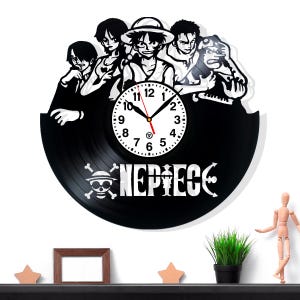 May include: Black vinyl record clock featuring a cartoon illustration of several characters. The clock face is white with black numbers and hands. The word "NEPIECE" is displayed in white below the clock face, with a skull and crossbones logo.