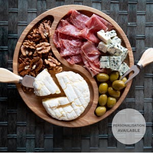 Peut inclure: Un plateau de service en bois avec trois sections, rempli de noix, de salami, de prosciutto, de fromage bleu, d'olives et d'un fromage blanc rond. Le plateau est sur une surface tissée. Personnalisation disponible.