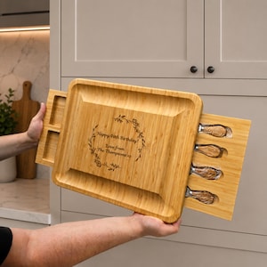 Peut inclure: Une planche de service rectangulaire en bambou avec un tiroir coulissant contenant quatre couteaux à fromage. Le centre de la planche présente un motif de couronne gravé au laser avec le texte : Happy 40th Birthday! Love from The Thompsons xx.