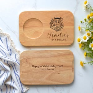 Puede incluir: Dos tablas de madera para servir té y galletas. Una tabla tiene una hendidura circular para una taza de té y el texto "Amelia's Tea & Biscuits". La otra tabla tiene el texto "Happy 60th birthday Dad! Love Emma".