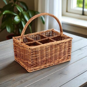 May include: A light brown woven wicker bottle carrier with a handle, designed to hold six bottles. The basket is rectangular and sits on a grey wooden surface. The handle arches over the top, and the interior is divided into compartments.