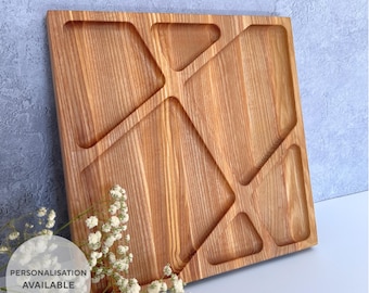 May include: A square wooden serving platter with geometric compartments. The light-coloured wood has visible grain and a central cross design. The text "PERSONALISATION AVAILABLE" is in a white circle in the lower left corner.