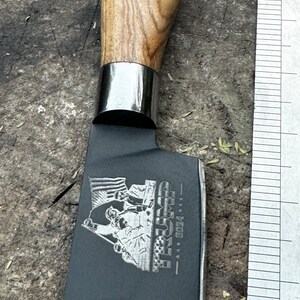 May include: A black cleaver knife with a wooden handle and a silver bolster. The blade features an engraved design with the text "TRUMP 2024" and an American flag.