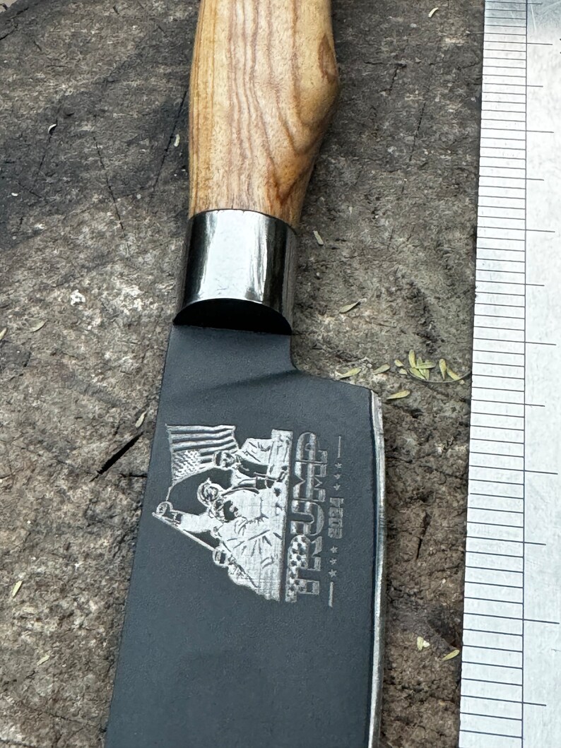 May include: A black cleaver knife with a wooden handle and a silver bolster. The blade features an engraved design with the text "TRUMP 2024" and an American flag.
