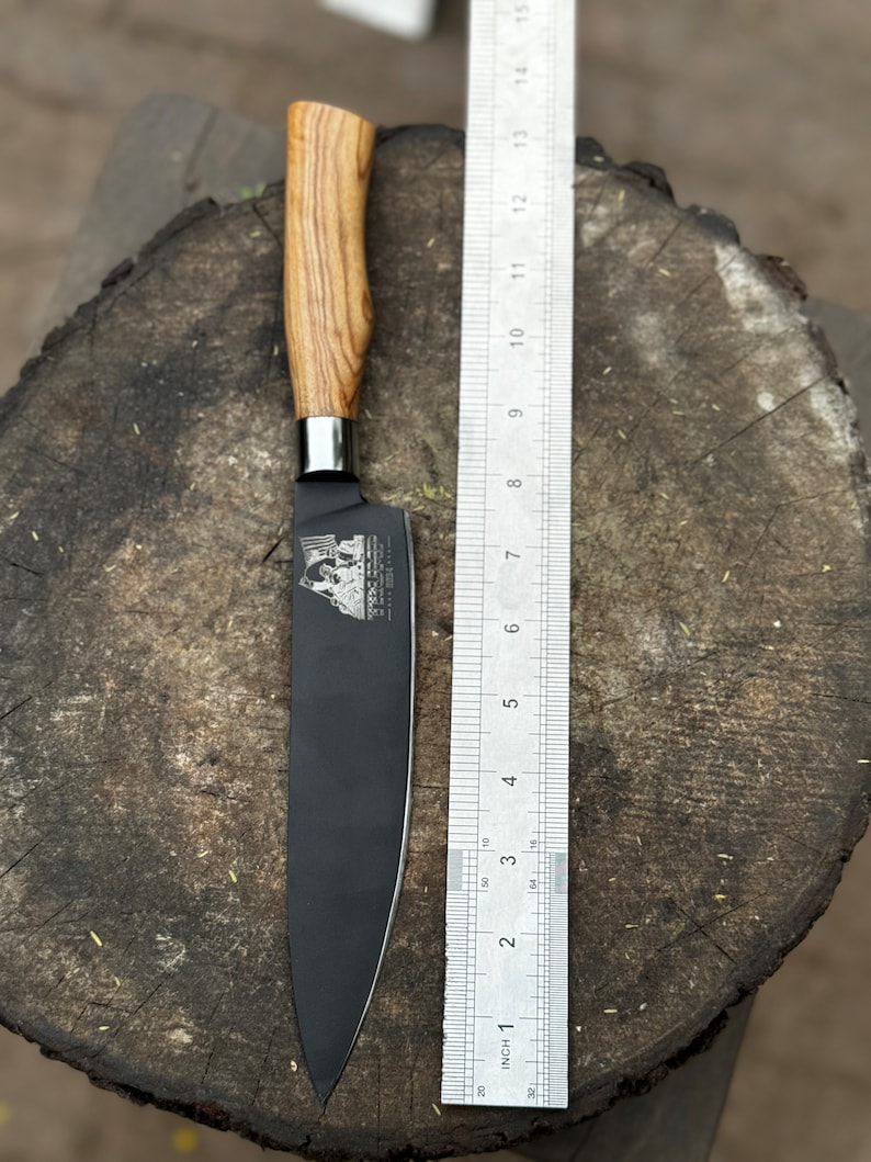 May include: A black chef's knife with a wooden handle, next to a ruler. The blade is approximately 10 inches long. The handle is light brown with a wood grain pattern. The knife is on a wooden surface.