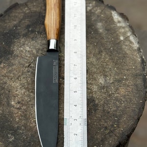 May include: A black chef's knife with a wooden handle and a stainless steel bolster. The blade is approximately 6 inches long, with the text "JW STEELCRAFTS" printed on the blade. A ruler is placed next to the knife for scale.