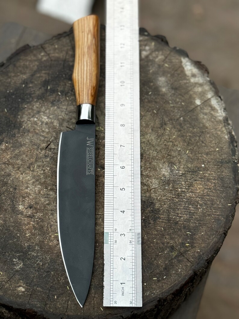 May include: A black chef's knife with a wooden handle and a stainless steel bolster. The blade is approximately 6 inches long, with the text "JW STEELCRAFTS" printed on the blade. A ruler is placed next to the knife for scale.
