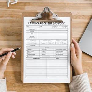 May include: A clipboard with a "LAWN CARE CLIENT LOG BOOK" form. The form includes fields for client information, job frequency, and services such as mowing, weeding, and tree trimming. A pencil is held in the left hand, ready to write.