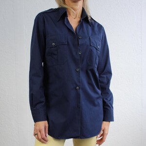 Può includere: Una camicia a maniche lunghe blu navy con colletto abbottonato e due tasche a patta. La camicia è realizzata in tessuto leggero e ha una vestibilità rilassata.