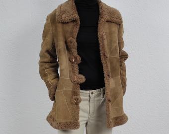 Puede incluir: Una chaqueta de ante y piel de oveja marrón con cuello alto y cierre de botones. La chaqueta se lleva sobre un jersey de cuello alto negro y unos vaqueros blancos.