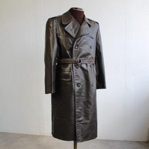 May include: A dark brown trench coat with a double-breasted design, a belt, and a classic collar. The coat is displayed on a vintage mannequin. The coat's length is approximately 140 cm.