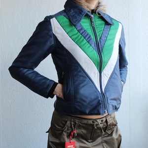 May include: A navy blue jacket with a green and white chevron design on the chest. The jacket has a zip-up front and a collar. The tag reads "MISS SIXTY".