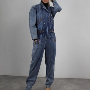 Könnte beinhalten: Ein blauer Jeans-Overall mit Knopfleiste vorne, langen Ärmeln und einem Gürtel in der Taille. Der Overall hat eine lockere Passform und ist aus einem weichen, bequemen Stoff gefertigt.