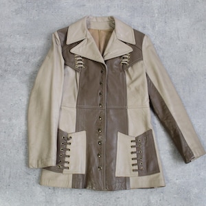 May include: A vintage leather jacket in a patchwork design. The jacket features a mix of beige and brown panels, with decorative lacing details on the pockets and front. It has a button-up closure and a classic collar, offering a retro aesthetic.