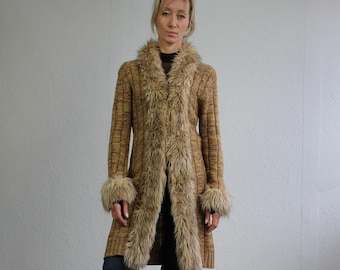 Könnte beinhalten: Ein langer brauner Cardigan mit einem Kragen und Ärmelbündchen aus Kunstpelz. Der Cardigan ist gestrickt und hat eine lockere Passform. Das Model trägt eine blaue Jeans und weiße Turnschuhe.