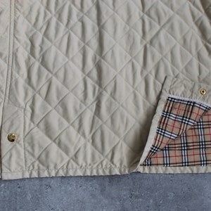 May include: A beige quilted jacket with a plaid lining. The jacket has a diamond quilted pattern and gold buttons.