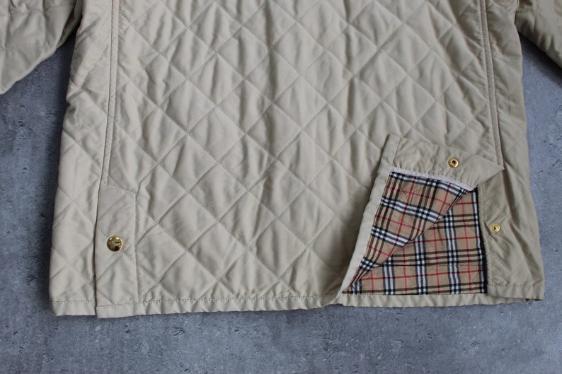 May include: A beige quilted jacket with a plaid lining. The jacket has a diamond quilted pattern and gold buttons.