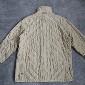 May include: A beige quilted jacket with a stand-up collar and a Burberry label on the back.