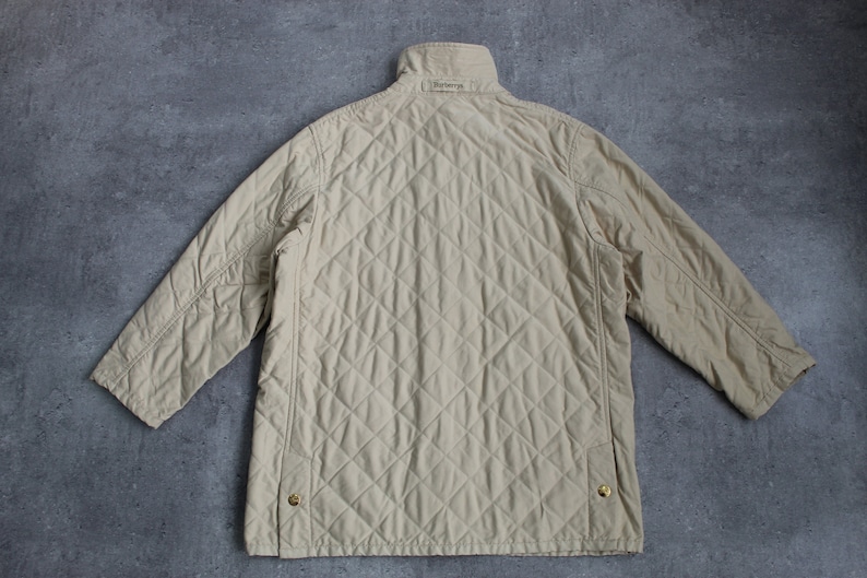 May include: A beige quilted jacket with a stand-up collar and a Burberry label on the back.