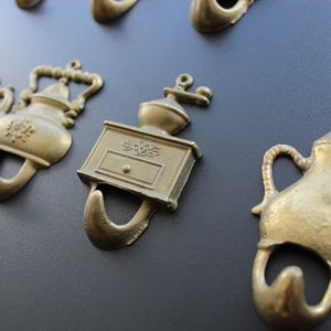 Puede incluir: Conjunto de ganchos de metal dorado en forma de cafeteras, teteras y molinillo de café. Los ganchos son decorativos y se pueden usar para colgar artículos en una pared.