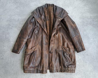 May include: A vintage brown leather coat with a hooded collar and button closure. The coat features two front pockets and a textured, worn appearance. The coat is a medium length.
