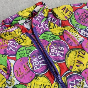 May include: A red, purple, yellow, and green patterned jacket with a zipper closure. The pattern features various state names and abbreviations, such as "Maryland", "Colorado", and "Washington", along with numbers and the word "PBK".