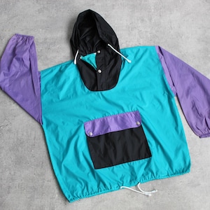 Może przedstawiać: Turkusowa, fioletowa i czarna kurtka z kapturem i sznurkiem do ściągania u dołu. Kurtka ma dużą kieszeń z przodu.