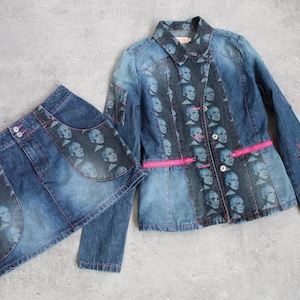 May include: A denim jacket and skirt co-ord set. The jacket has a pink zip and button closure. Both items feature a repeating face print in blue and grey. The denim is a medium wash with pink stitching.