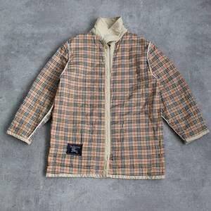May include: A beige quilted jacket with a plaid pattern in black, red, and white. The jacket has a zipper closure and a stand-up collar. The label on the jacket reads "Burberrys".