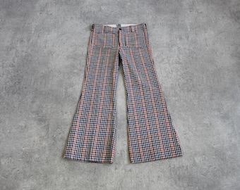 May include: A pair of vintage bell-bottom pants. The pants feature a checkered pattern in red, navy blue, and white. The pants are laid flat on a gray surface, showcasing the flared leg design.