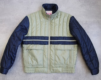 May include: A green and navy blue quilted jacket with a zipper closure and two flap pockets. The jacket has a stand-up collar and a white label with the text "Wonderland" on the front.