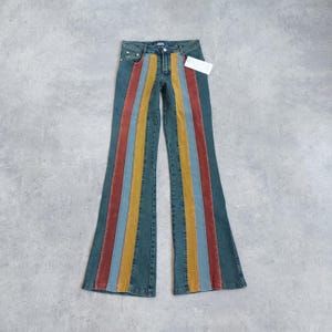May include: Blue denim flared jeans with vertical stripes in red, yellow, and blue. The jeans have a high waist and a tag attached. The colorful stripes run down the front of each leg, creating a retro look.