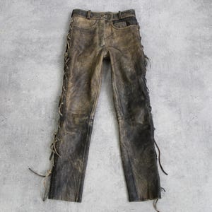 Pode incluir: Calça de couro marrom com cadarços nas laterais. A calça tem um visual desgastado e é amarrada na parte inferior.