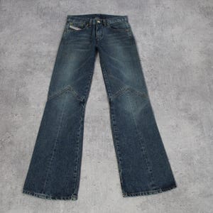 May include: Blue denim jeans with a flared leg design. The jeans have a classic five-pocket style, a button and zipper closure, and a small logo detail on the front pocket. The jeans are laid flat on a gray surface.