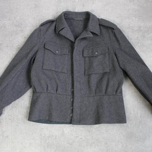 May include: A gray wool jacket with a button-up front and two large flap pockets. The jacket has a cinched waist and long sleeves.