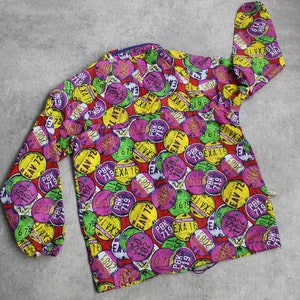 May include: A colorful button-down shirt with a pattern of various license plates. The plates are in shades of red, yellow, green, and purple, with black numbers and letters. The shirt has a long sleeve and a button-up front.