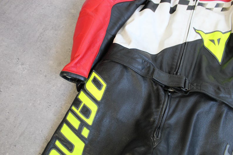 May include: Black and red leather motorcycle suit with white and black checkered accents. The suit features a yellow logo and lettering. The suit has a zipper closure and a belt.