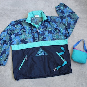 Puede incluir: Chaqueta anorak vintage azul, turquesa y marino con un patrón geométrico. La chaqueta tiene media cremallera, una banda en el pecho turquesa y una pequeña bolsa turquesa con una correa azul. El texto "ANTEX" es visible.