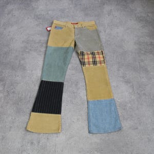 May include: Multi-fabric patchwork jeans with a flared leg. The jeans combine denim, corduroy, and plaid in shades of tan, blue, grey, and black. The trousers have a unique, eye-catching design.