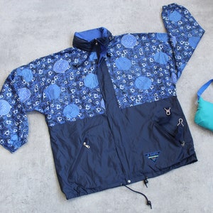 Puede incluir: Una chaqueta con estampado azul y negro con cierre de cremallera y capucha con cordón. La chaqueta tiene un logotipo en la parte inferior izquierda que dice "A. Barrie".