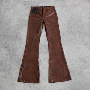 Puede incluir: Pantalones acampanados marrones con un patrón texturizado similar a la piel de serpiente. Los pantalones tienen una cintura alta y una etiqueta adjunta en la parte superior. Los pantalones se muestran sobre una superficie gris.