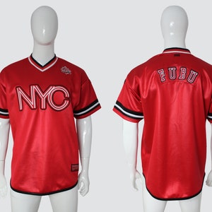 May include: Red baseball jersey with black and white trim. The front of the jersey has a white "NYC" graphic. The back of the jersey has "FUBU" in white lettering.
