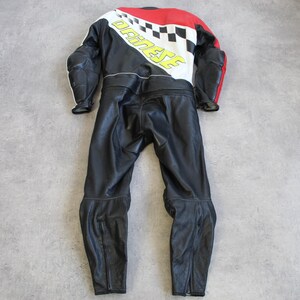 May include: Black and red motorcycle racing suit with white and yellow accents. The suit features a checkered design and the brand name "DAINESE" in yellow. The suit is made of leather and has protective padding on the shoulders and elbows.